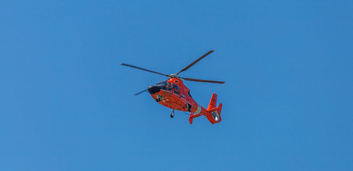 Red helicopter in a low-angle shot soaring against a clear blue sky
